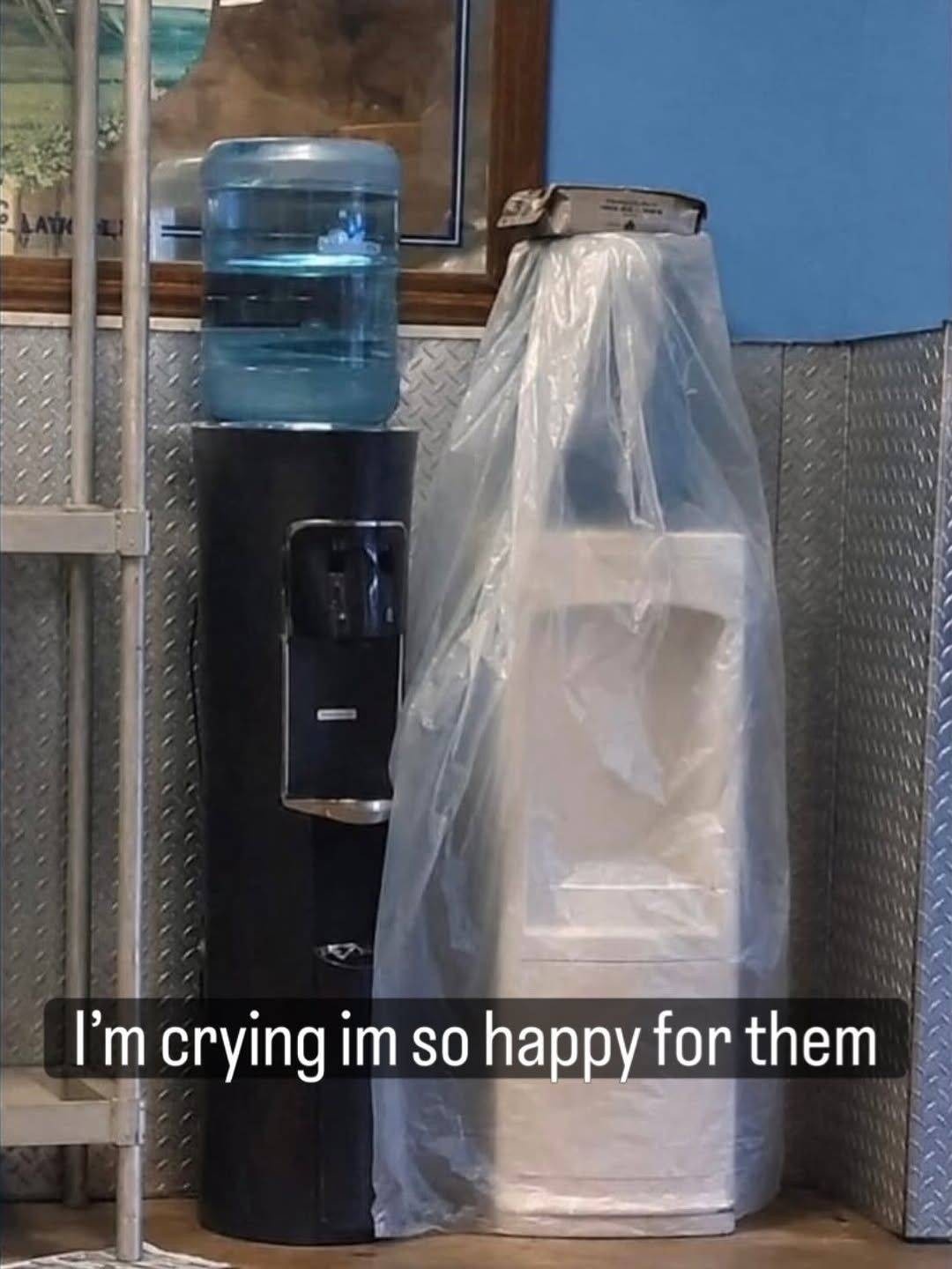 Black water dispenser and a white water dispenser under plastic, they look like a couple that is getting married. The caption reads: "I'm crying im so happy for them"